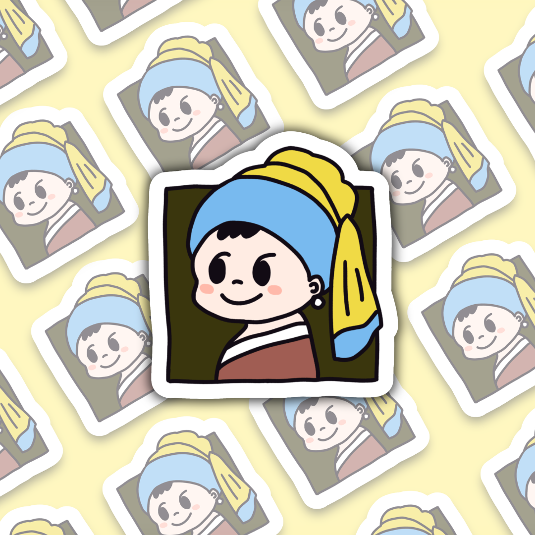 Hand holding a small cartoon sticker inspired by "Girl with a Pearl Earring," featuring a cute character with a blue headscarf and yellow details, against a blurred indoor background.